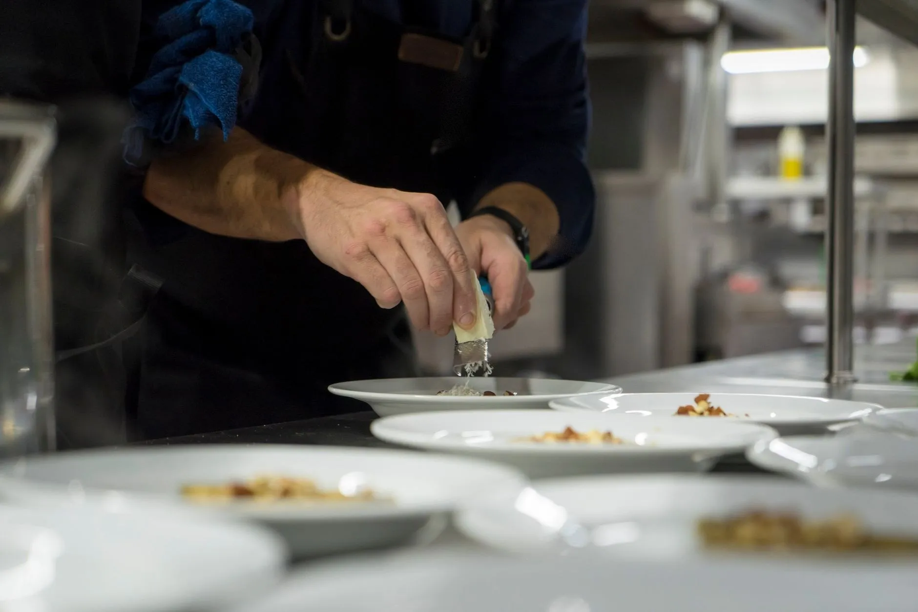A chef grating a finish over plates lined up on a kitchen pass