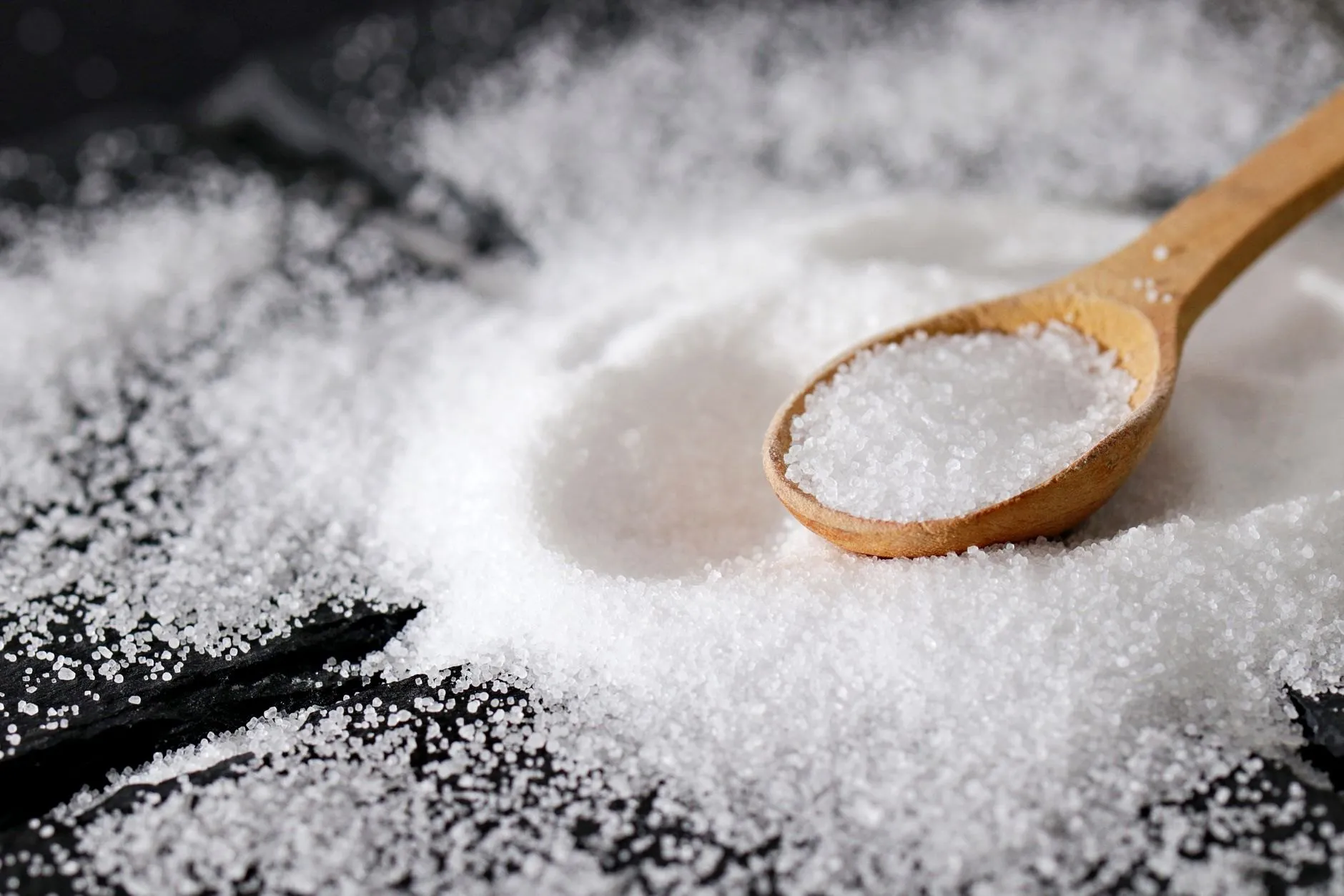 Fine sea salt spilled across black slate with a wooden spoon