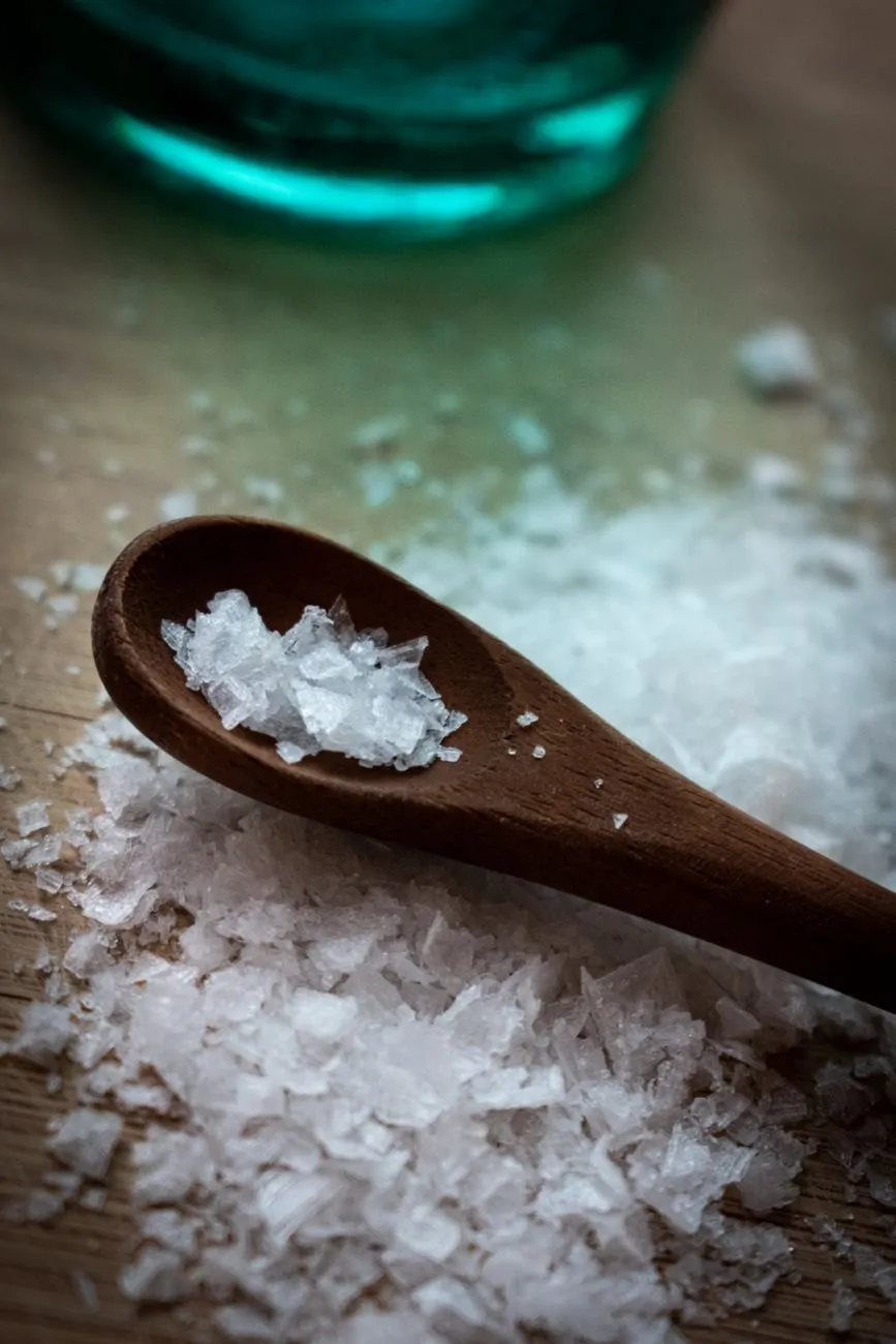 Large translucent sea salt flakes in a dark wooden spoon