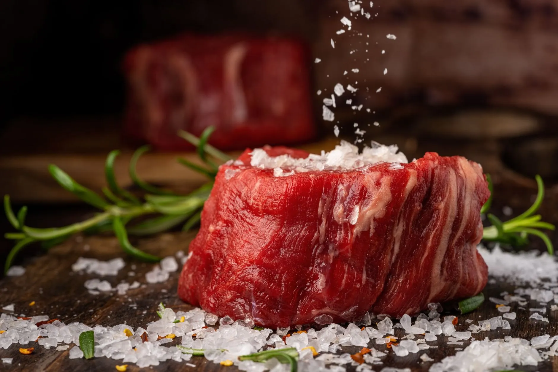 Salt flakes falling onto a thick raw fillet steak with rosemary